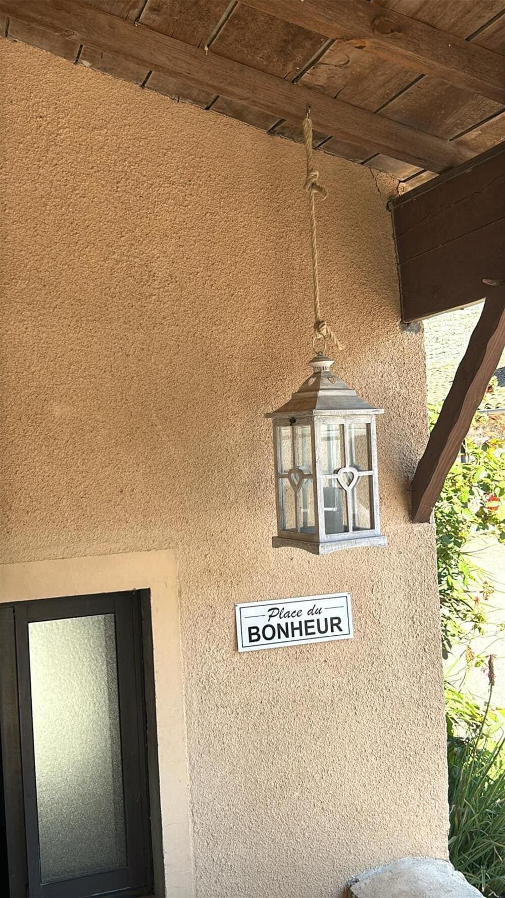 Une charmante lanterne suspendue par une corde à un toit, créant une ambiance chaleureuse et lumineuse au Domaine du Vieux Lavoir. Juste derrière, une pancarte accrochée au mur proclame 'La Place du Bonheur', un message qui incarne parfaitement l'esprit de notre domaine. Ce détail décoratif symbolise l'atmosphère joyeuse et mémorable que nous offrons pour vos mariages et grandes réceptions dans les Deux-Sèvres, où chaque recoin invite à la célébration et au bonheur.