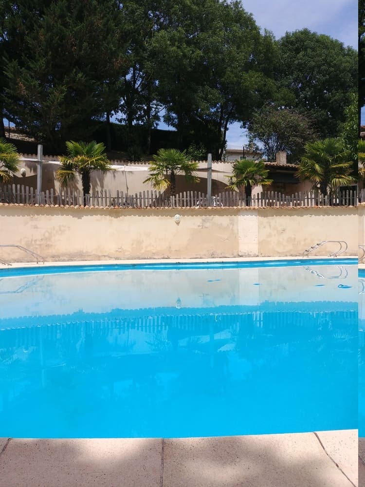 La magnifique piscine du Domaine du Vieux Lavoir au premier plan, avec en arrière-plan la terrasse ombragée située juste au-dessus. Cet espace idyllique offre un lieu parfait pour la détente et le rafraîchissement des invités de vos mariages et grandes réceptions dans les Deux-Sèvres, permettant de profiter pleinement du cadre ensoleillé tout en bénéficiant d'un abri confortable.