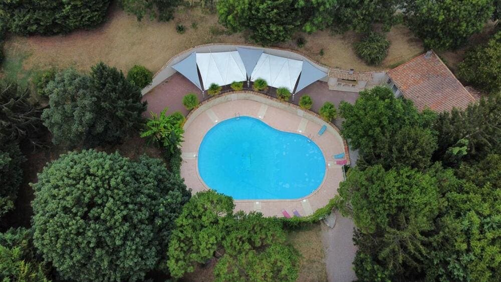 Vue aérienne spectaculaire de la grande piscine du Domaine du Vieux Lavoir, capturée par drone. Cette perspective unique révèle la piscine elle-même, la terrasse ombragée élégamment aménagée avec ses voiles, ainsi que le pool-house attenant. Cet ensemble forme un espace de loisirs et de détente privilégié pour vos invités, ajoutant une touche de luxe et de convivialité à vos mariages et grandes réceptions dans les Deux-Sèvres.