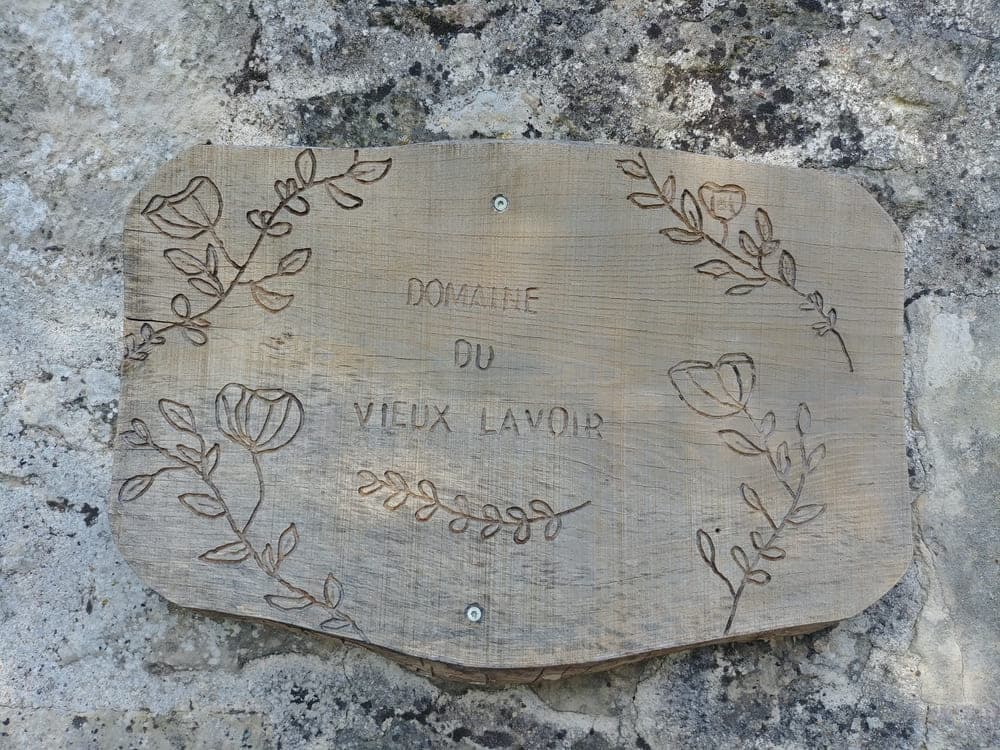 Une charmante pancarte en bois faite maison , gravée de délicates fleurs et du nom 'Domaine du Vieux Lavoir'. Cet élément décoratif unique, empreint d'authenticité, accueille chaleureusement les visiteurs et reflète le soin apporté à chaque détail de notre propriété. Il symbolise l'esprit convivial et le cadre naturel que nous offrons pour vos mariages et grandes réceptions dans les Deux-Sèvres, invitant à découvrir un lieu où l'artisanat et la nature se rencontrent.