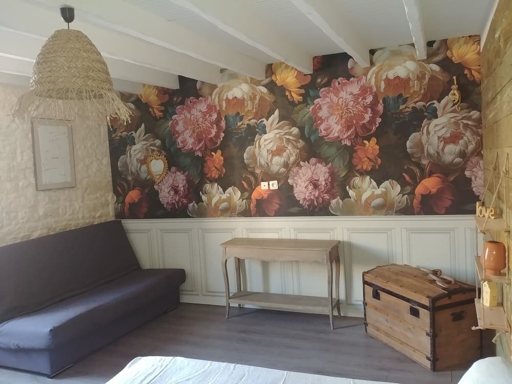 Autre vue de la chambre au rez-de-chaussée du Gîte Pivoine au Domaine du Vieux Lavoir, révélant un confortable canapé et une élégante tapisserie fleurie. Ces détails décoratifs ajoutent au charme et au confort de la pièce, offrant un espace douillet pour se détendre. Cette chambre, avec son lit double, est idéale pour les invités de vos mariages et grandes réceptions dans les Deux-Sèvres, combinant esthétique et fonctionnalité.
